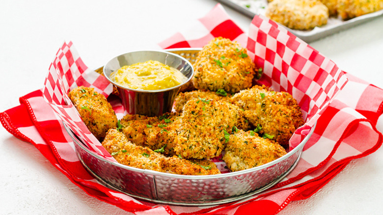 metal basket filled with air fryer chicken nuggets and a container of dipping sauce