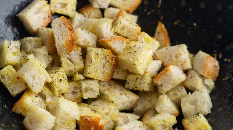 seasoning croutons with olive oil and seasonings in bowl