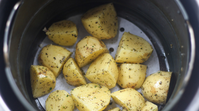 Chopped up raw potatoes covered in oil and spices sitting in an air fryer