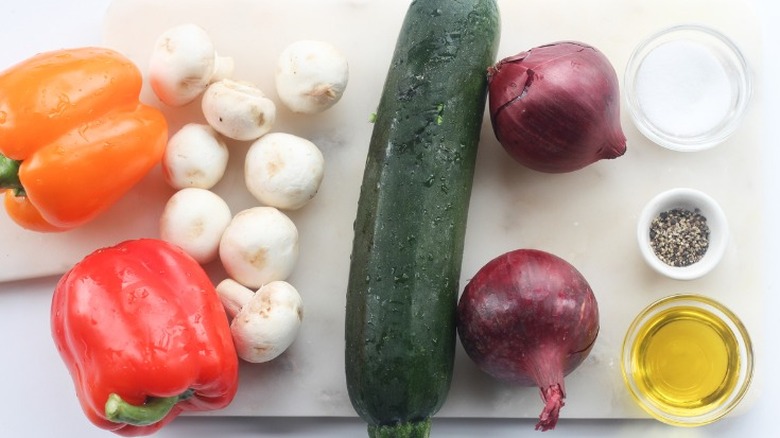 bell peppers, mushrooms, red onions, and zucchini on cutting board with oil, salt, and pepper