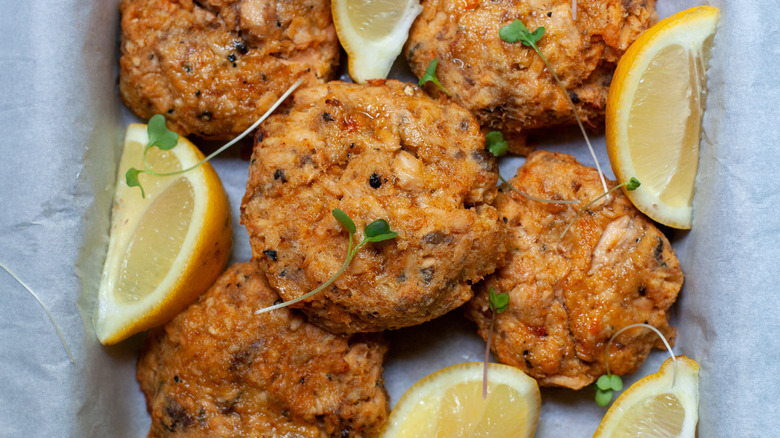 Salmon patties sit alongside lemon wedges with microgreens