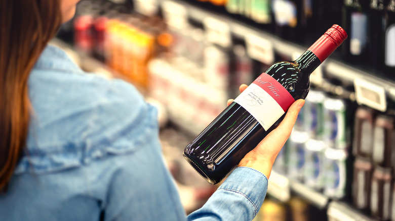 person holding bottle of red wine in alcohol section of store