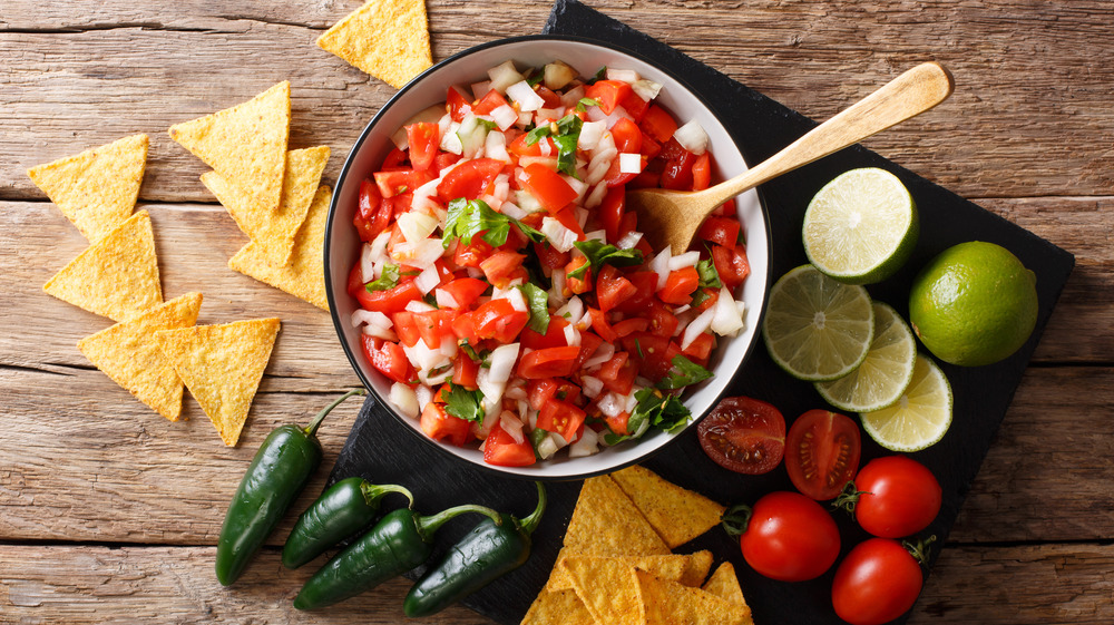 Bowl of pico do galllo next to vegetables and chips