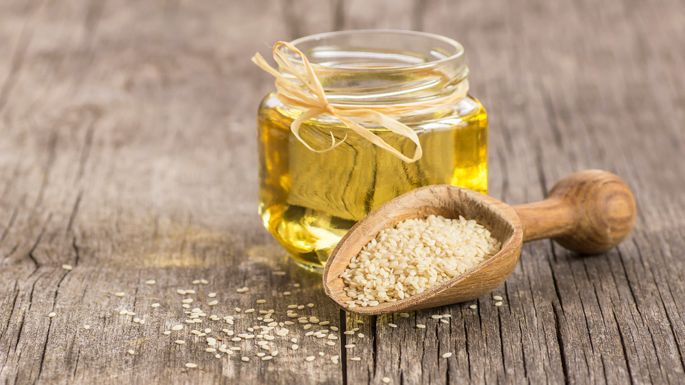 Jar of sesame oil and seeds on wooden table