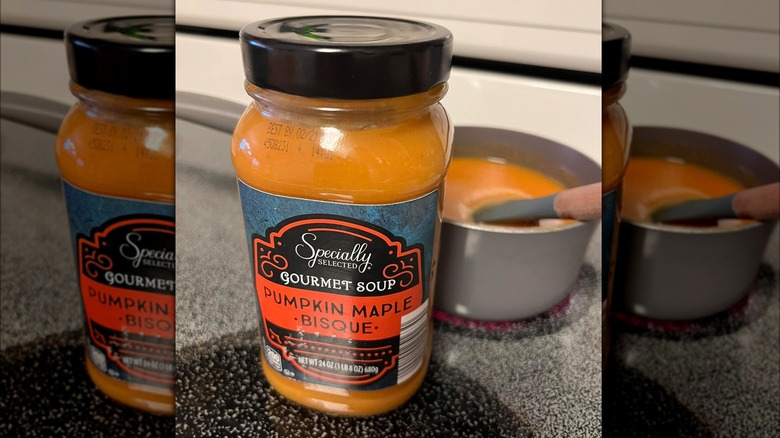 Jar of Aldi's pumpkin maple bisque next to pot on stove