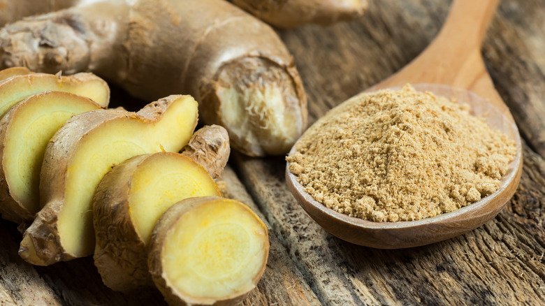 Ground ginger in a wooden spoon next to fresh ginger