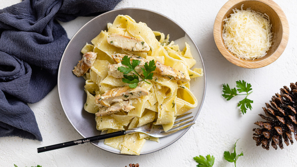 Chicken Alfredo on patterned plate with bowl of parmesan and blue towel