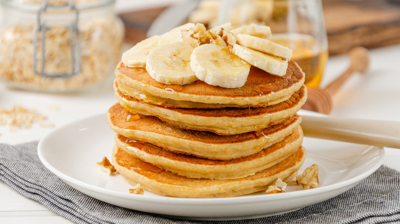 Stack of pancakes with sliced banana, maple syrup and chopped walnuts