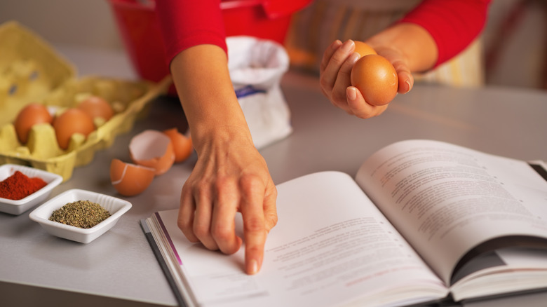 person looking at recipe holding egg