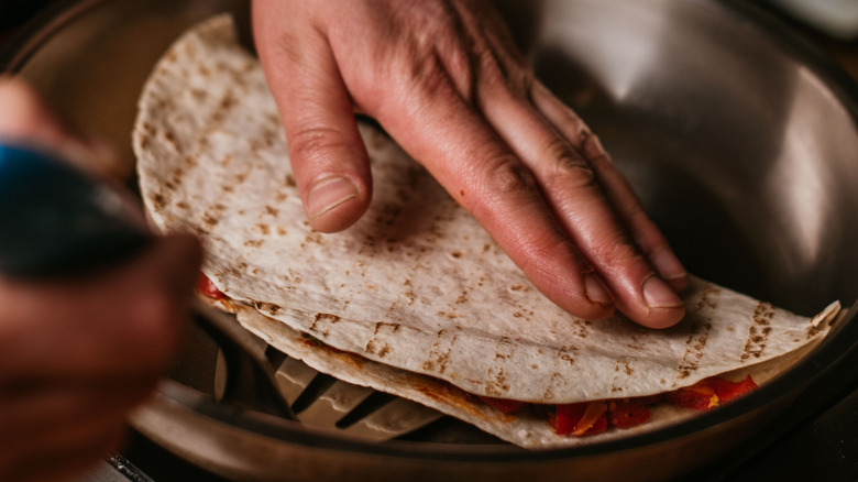 Person cooking quesadilla in pan