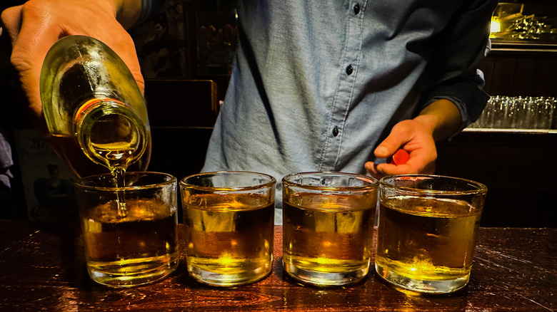 man pouring four whiskeys