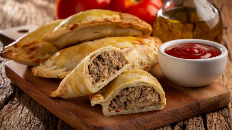 empanadas with beef filling and red sauce on cutting board