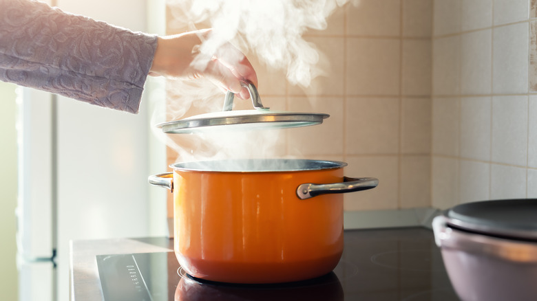 Person pulling lid off of steaming pot filled with hot water 