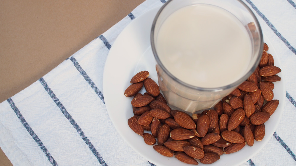 Almond milk with almonds touching the glass 