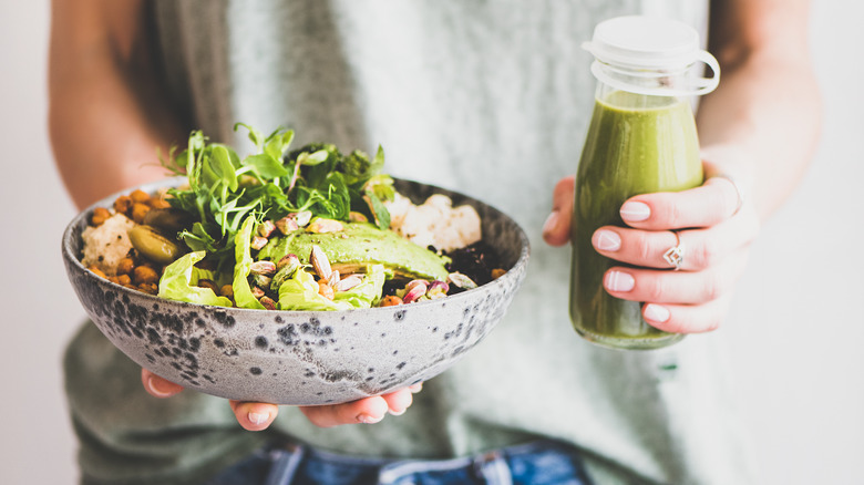 Person holding salad bowl and green smoothie