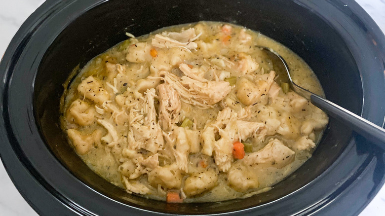 shredded chicken and dumplings with herbs and veggies in slow cooker with spoon