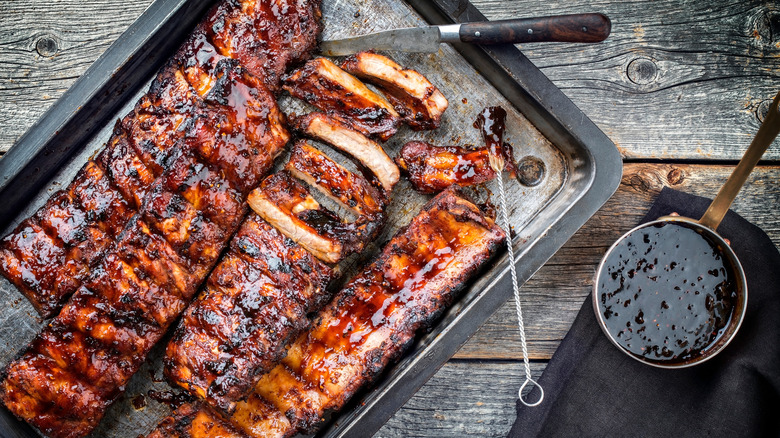Rack of St Louis ribs sit on a tray with a knife and barbecue tools 
