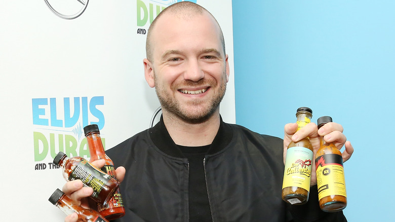 Sean Evans holding up hot sauces