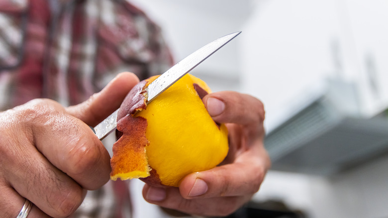 Man paring a peach with a knife