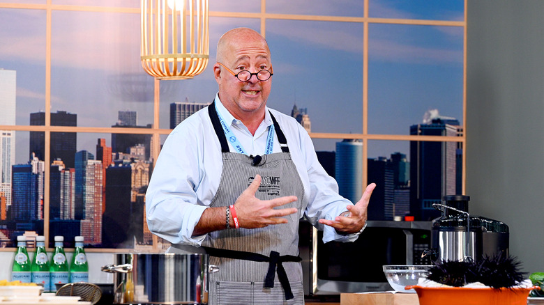 Andrew Zimmern behind a kitchen island making hand motions