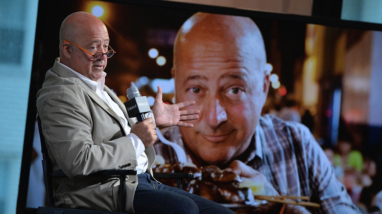 Andrew Zimmern with an episode of Bizarre Foods next to him onscreen 