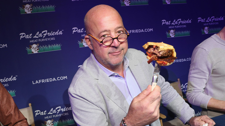 Andrew Zimmern holding up a partially eaten burger 