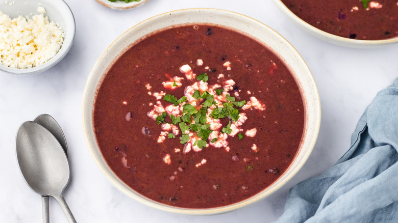 Bowl of purple black bean soup garnished with crumbled feta and cilantro