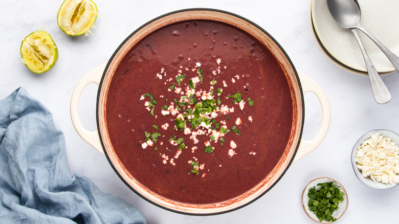 Purple black bean soup in pot with crumbled feta cheese and cilantro garnish