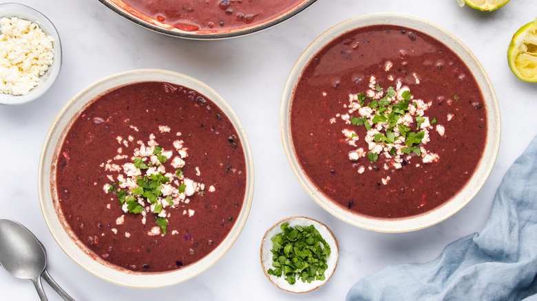 Two bowls of purple black bean soup garnished with feta and cilantro