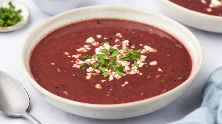 Bowl of purple black bean soup garnished with feta and cilantro