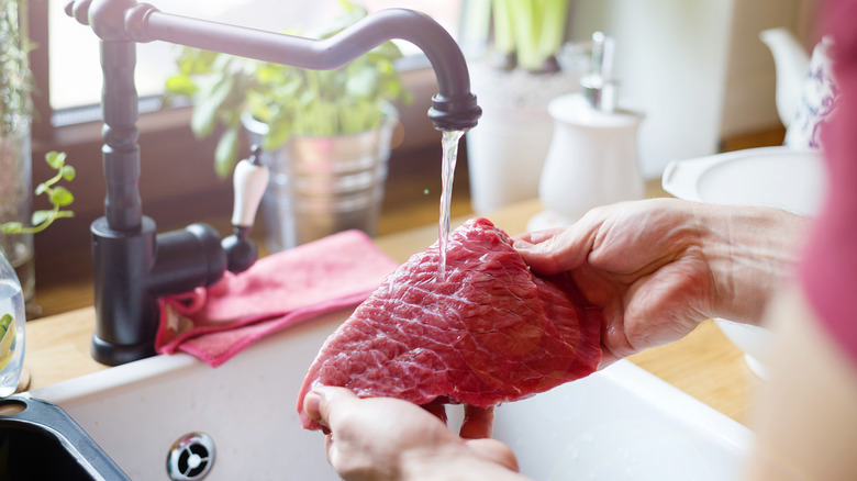 hands rinsing meat under faucet