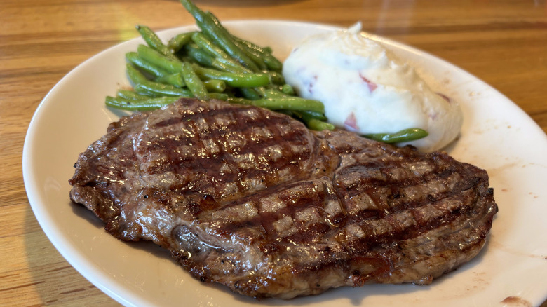 Ribeye steak on plate with green beans and mashed potatoes