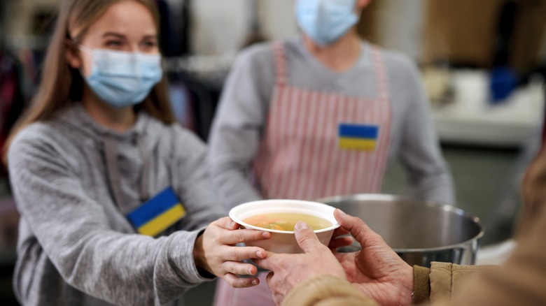 food bank volunteer gives soup to hungry person