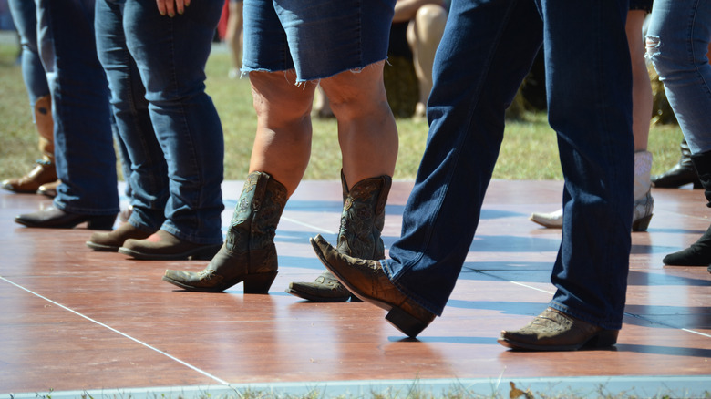 Men and women from legs down wearing boots, line dancing