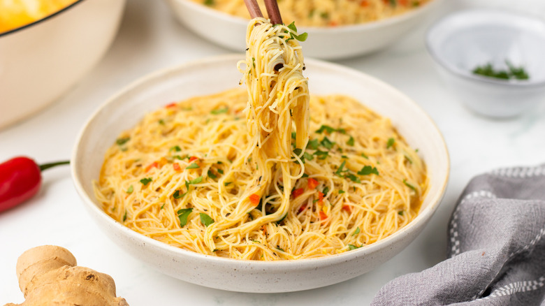 Lifting coconut curry noodles from bowl with chopsticks