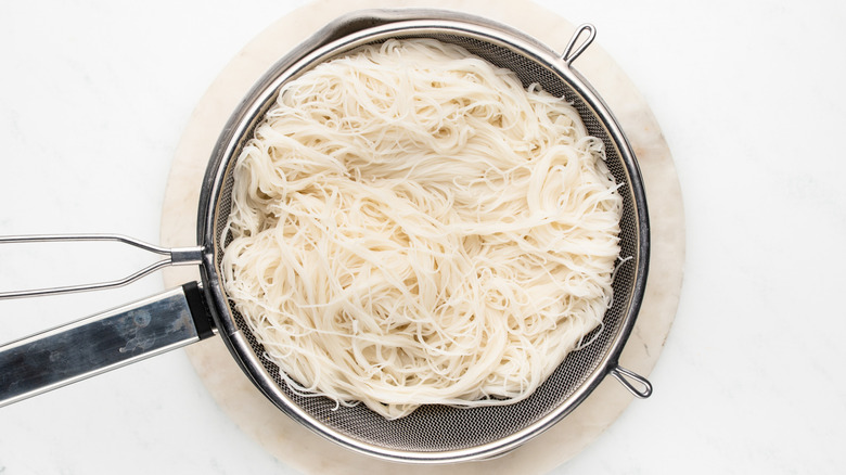 Rice noodles draining in sieve over saucepan