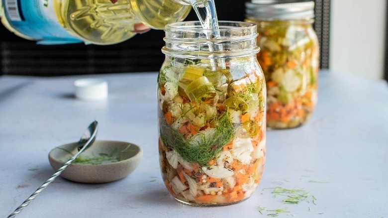 pickled vegetables and fennel being covered with soybean oil in a mason jar