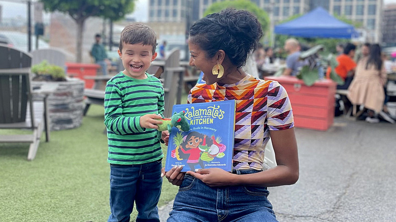 Sarah Thomas holding book and kneeling with child