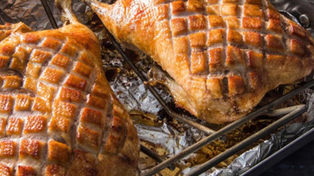 Close-up of two whole roasted ducks with diamond pattern cut into skin.