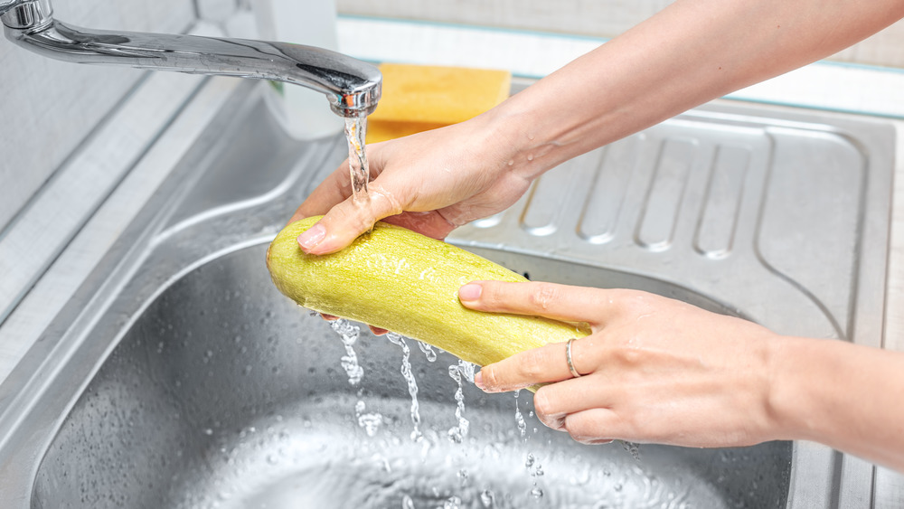 Hands holding zucchini as water washes it