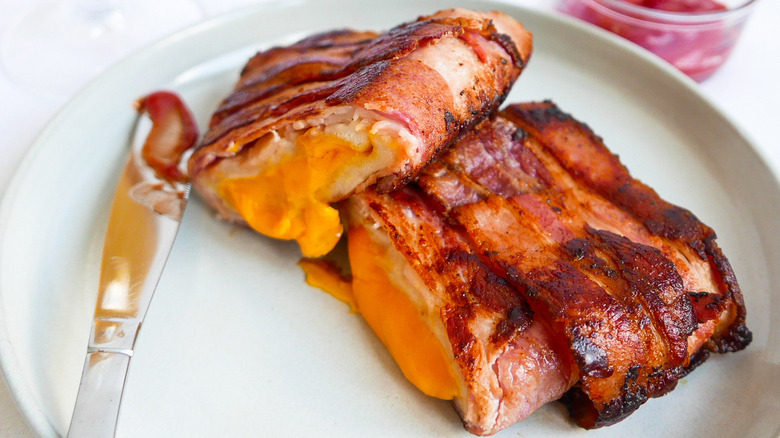 Bacon wrapped grilled cheese sits on a plate with a butter knife