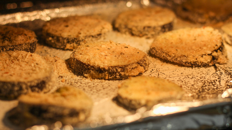 Breaded eggplant discs on a lined baking tray inside the oven.