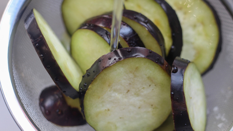 Eggplant discs in a colander and placed under running water.