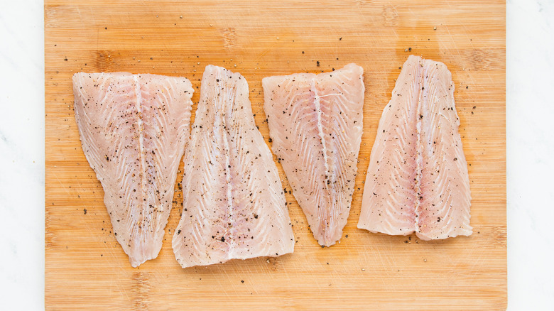 Seasoned tilapia fillets on wooden board