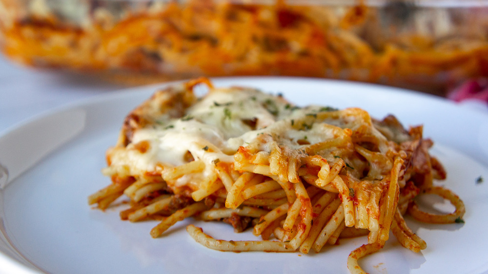 a white plate with a single portion of baked spaghetti in front of the casserole dish