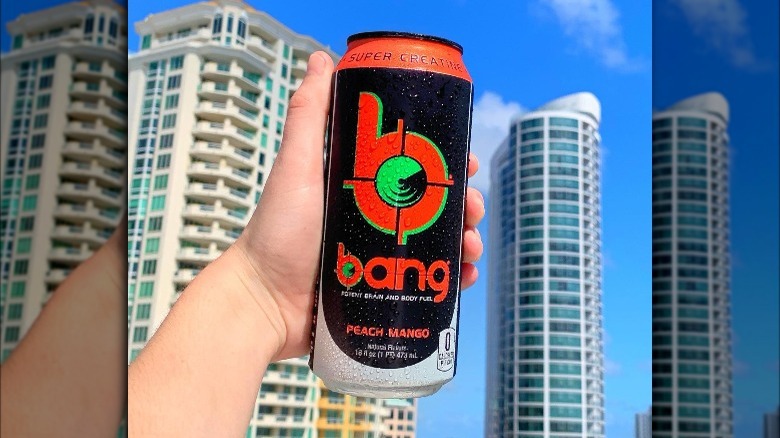 Someone holding can of Bang Energy Peach Mango with skyscrapers in background