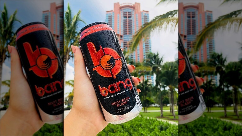 Someone holding Bang Energy Root Beer Blaze in front of skyscrapers