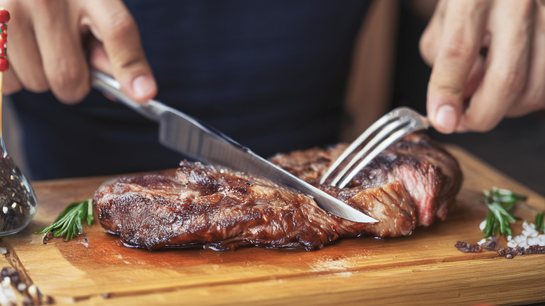Person slicing steak on cutting board