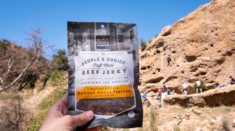 Someone holding People's Choice Beef Jerky with rock climbing background
