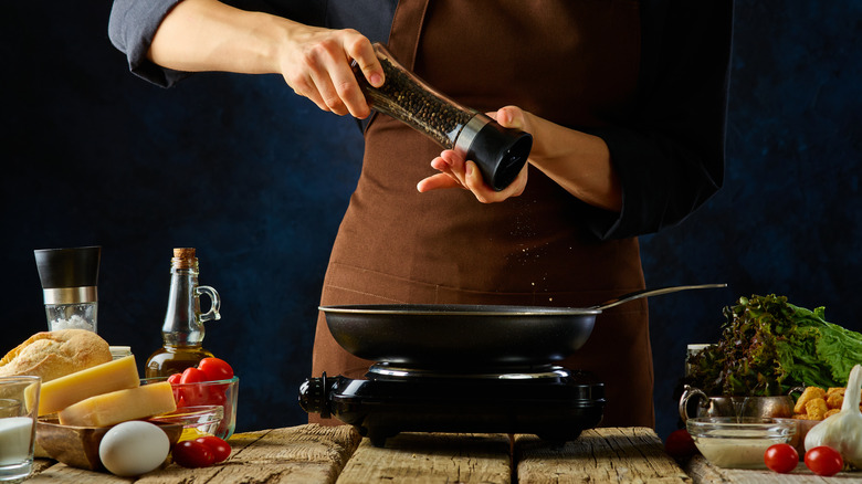 chef adding black pepper to pan